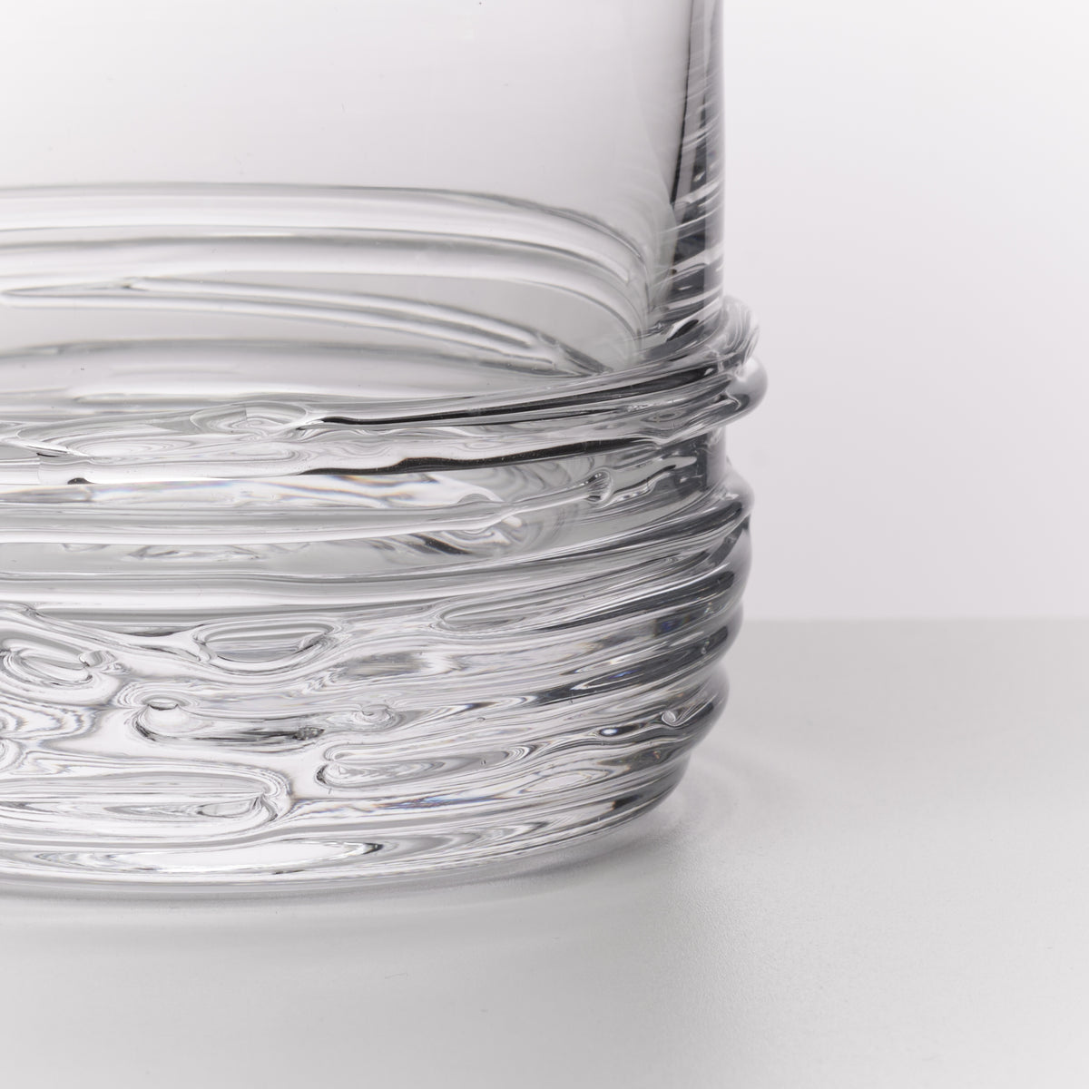 Close-up of a clear ribbed glass container or vase showing the textured transparent base against a light gray background.