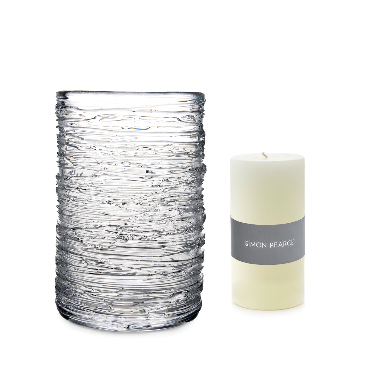 Clear glass hurricane vase with textured surface next to cream pillar candle with gray Simon Pearce band.