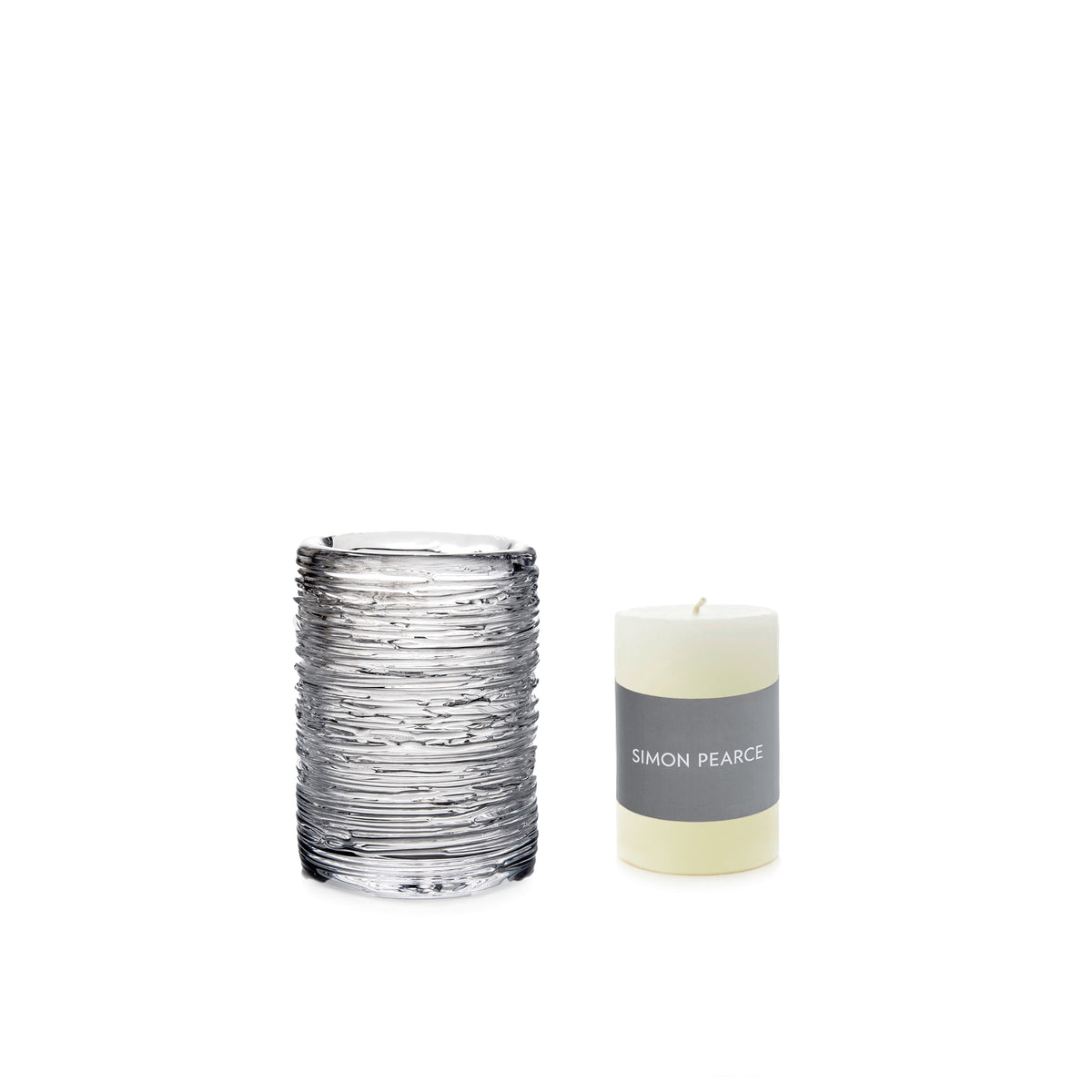 Cream pillar candle with gray band label next to textured glass hurricane holder.