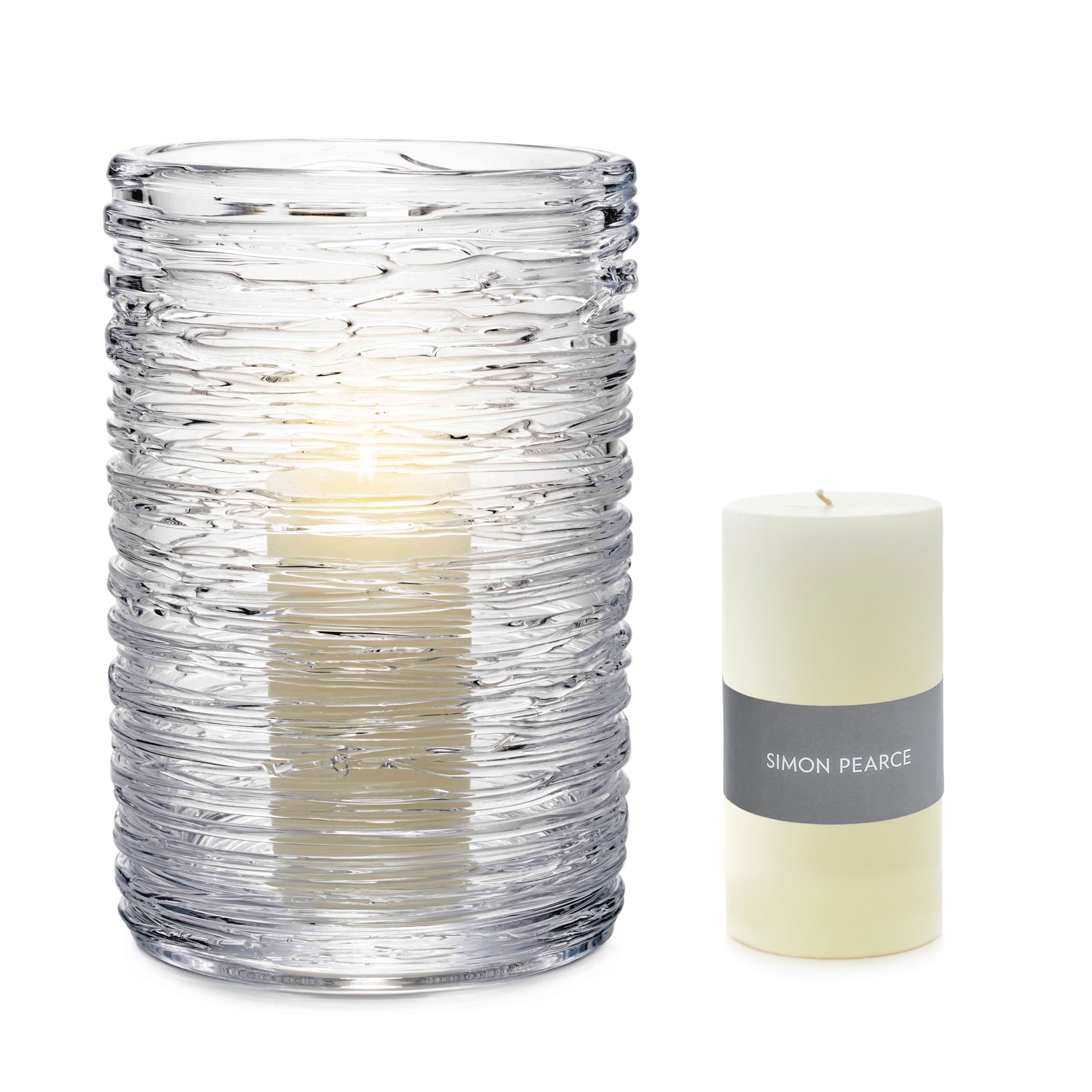 Clear textured glass hurricane vase with cream-colored pillar candle labeled Simon Pearce beside it.