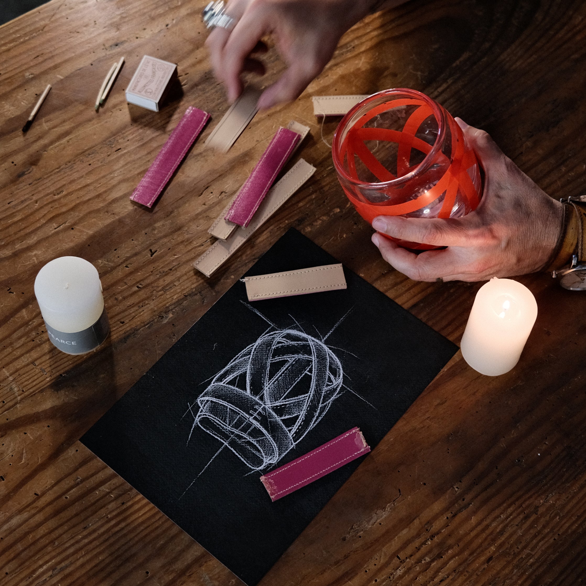 Burgundy leather wrap with white stitching displayed on black packaging, surrounded by craft materials and candles on wooden 