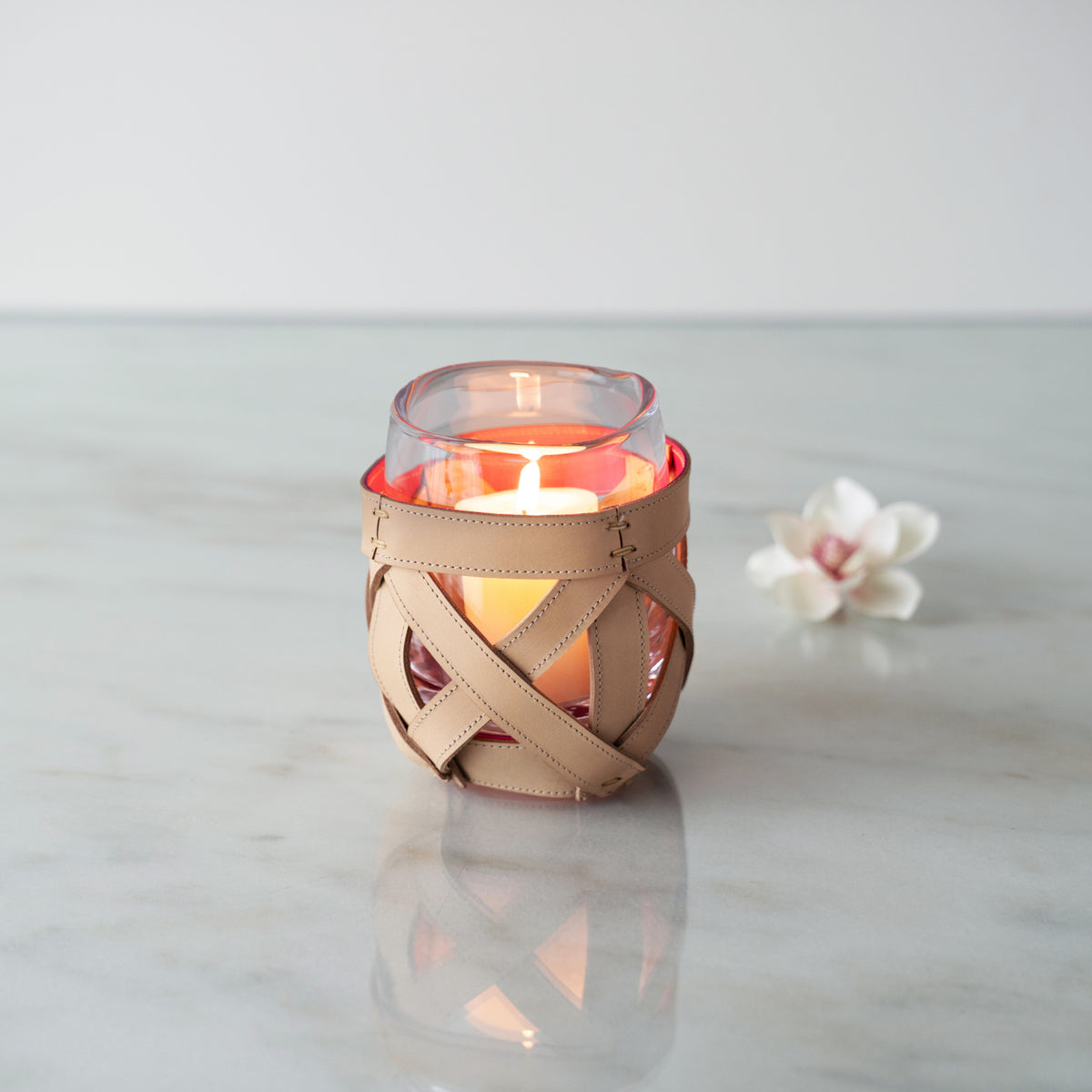 Tan leather wrap with cutout details around a glass candle holder containing red and yellow layers.