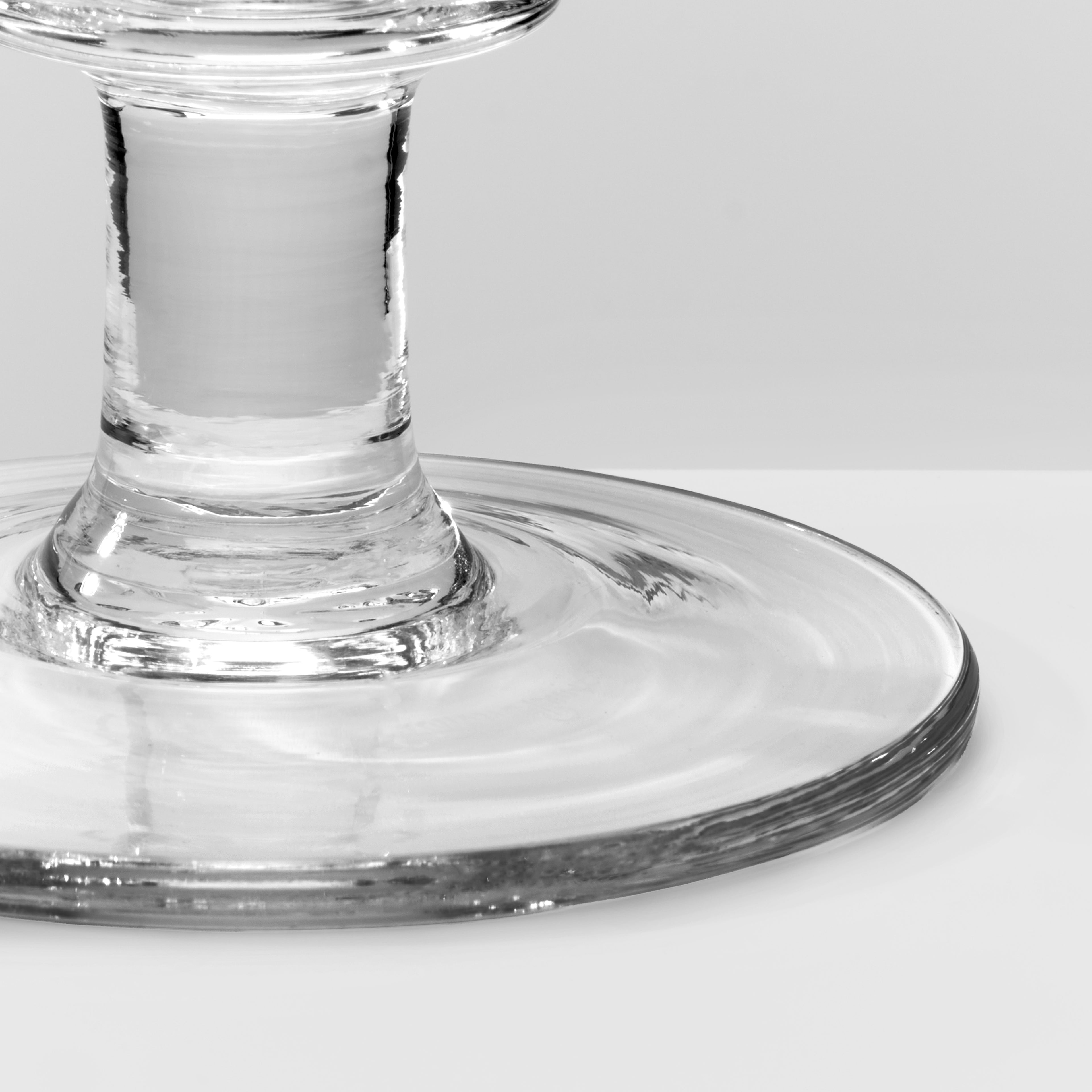 Close-up of a clear glass pedestal base with a wide circular foot, photographed on a light gray background.