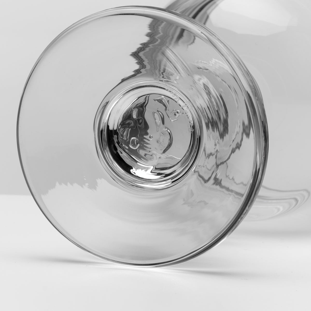 A close-up studio shot of a clear glass viewed from the base, showing the circular glass body and subtle reflections on a light gray background.