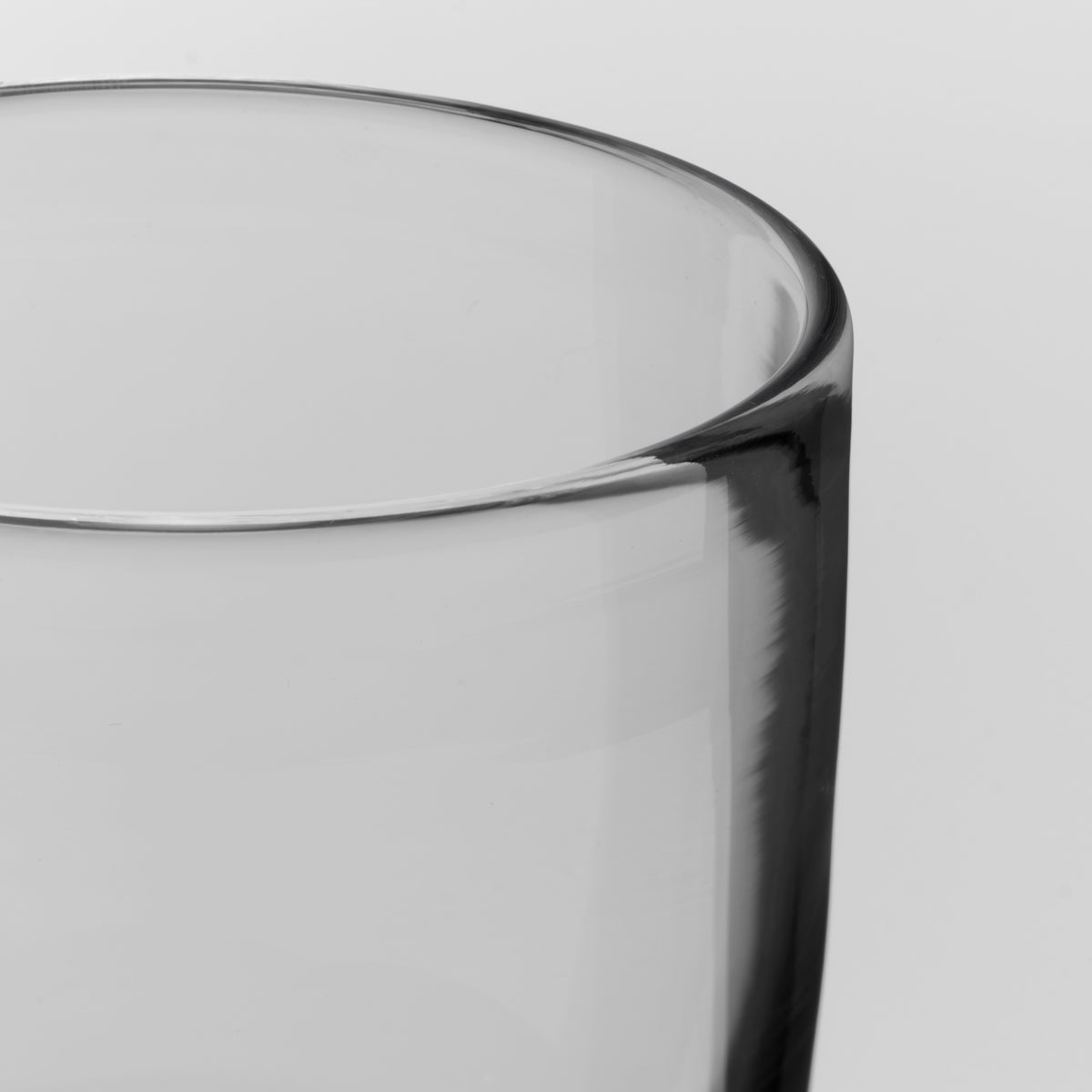 Close-up of a clear glass tumbler showing the rim and side profile against a light gray background.