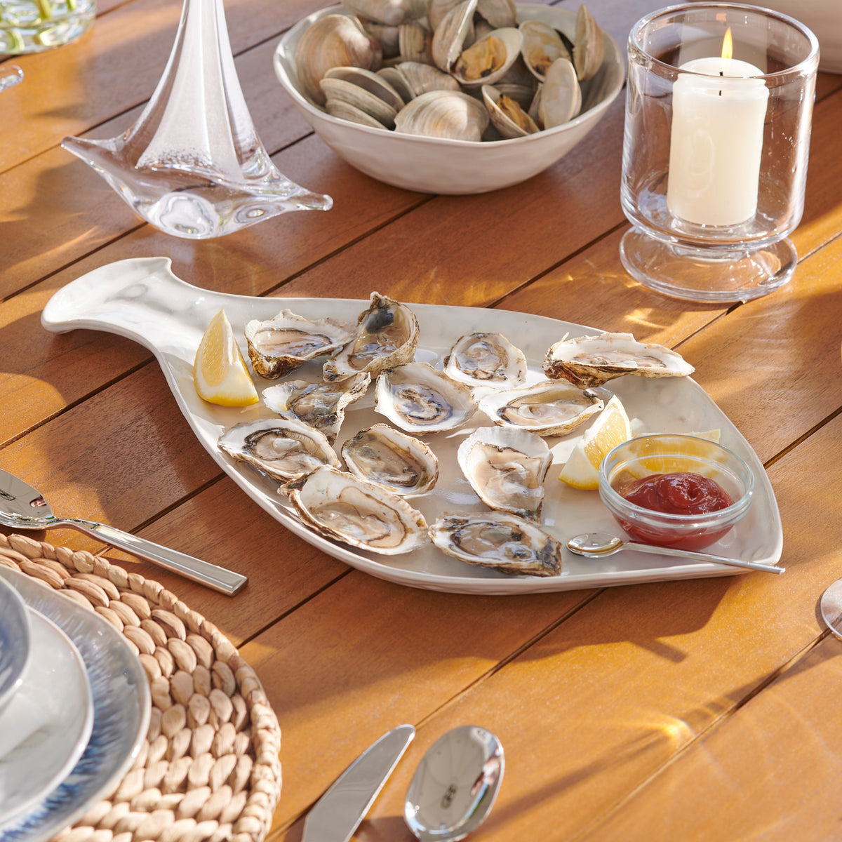 White fish-shaped platter filled with oysters, lemon wedges, and cocktail sauce on a wooden table.