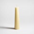 Cream-colored pillar candle with vertical fluted grooves and a wick at the top.