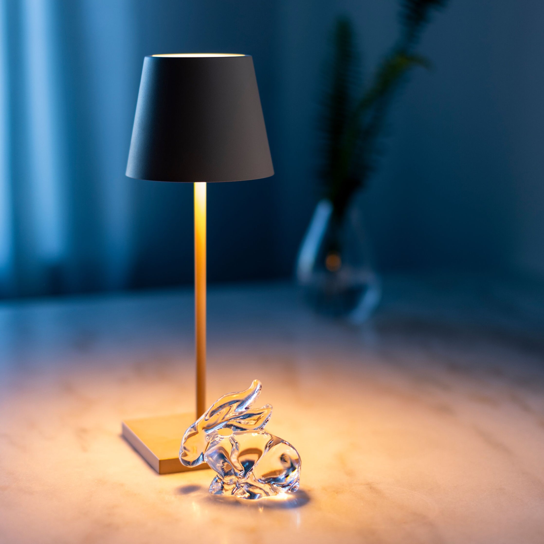 Table lamp with black conical shade and gold stem, featuring illuminated glass rabbit figurine base.