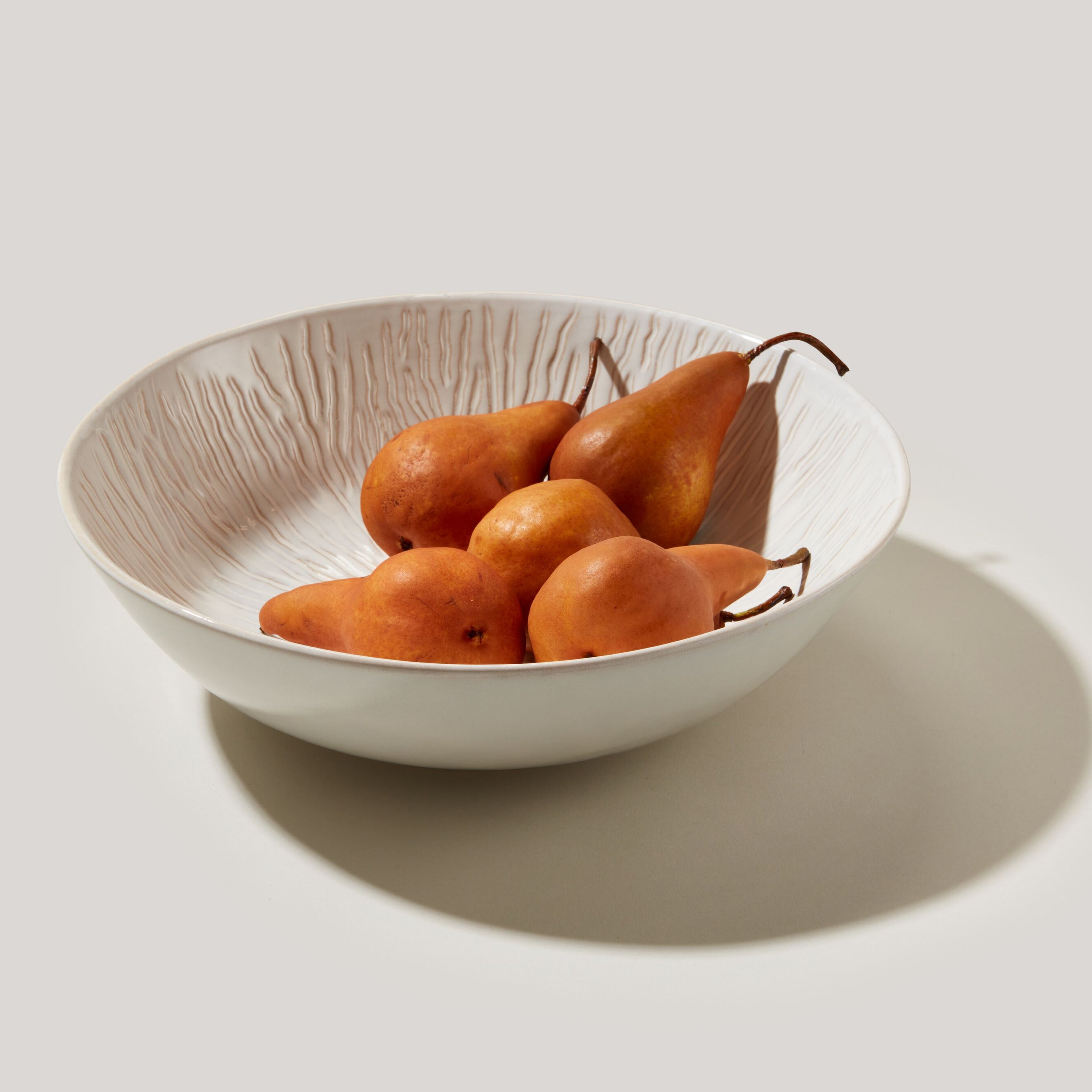 Cream-colored ceramic serving bowl with textured interior, filled with brown pears.