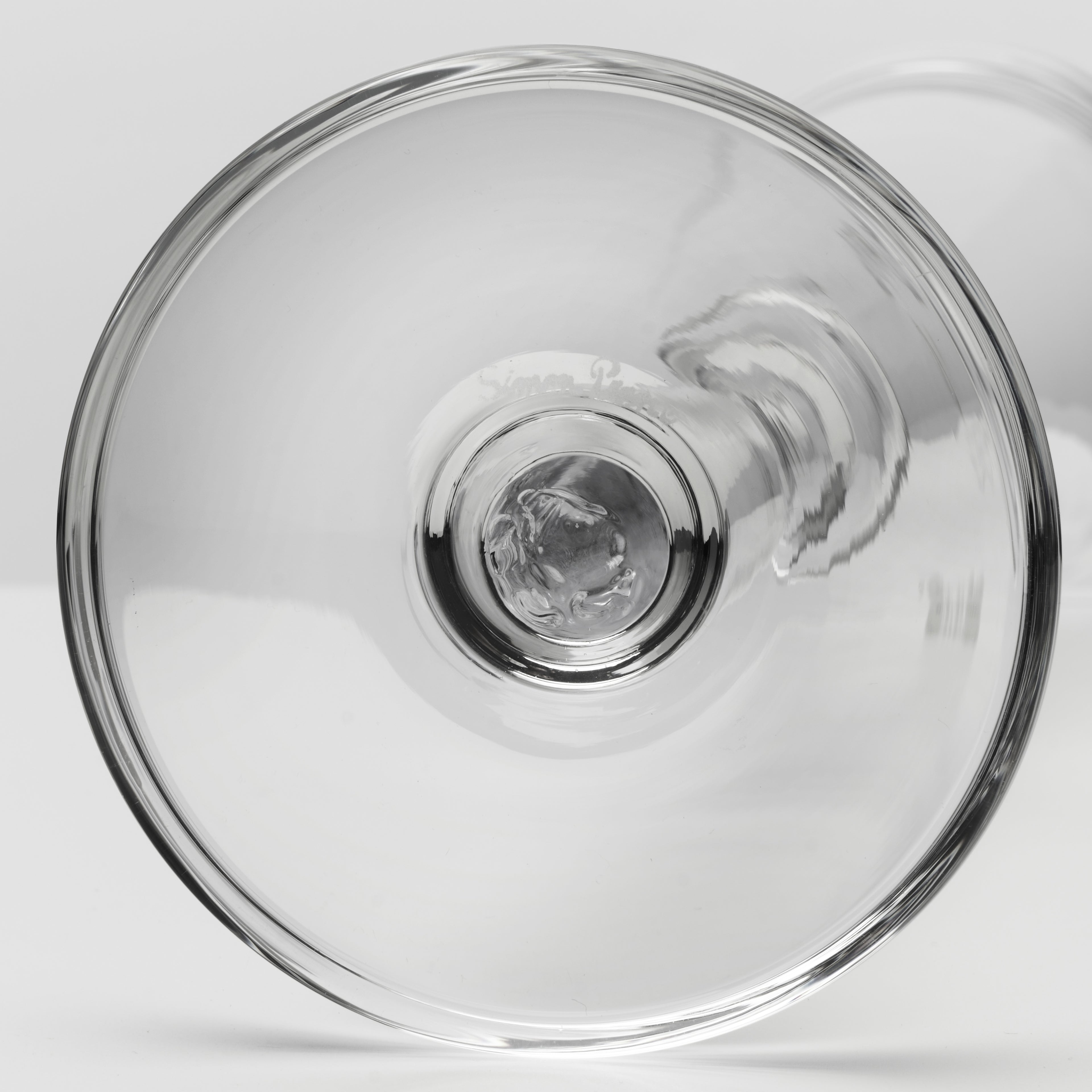 A close-up studio shot of a clear glass product, shown from above against a light gray background.