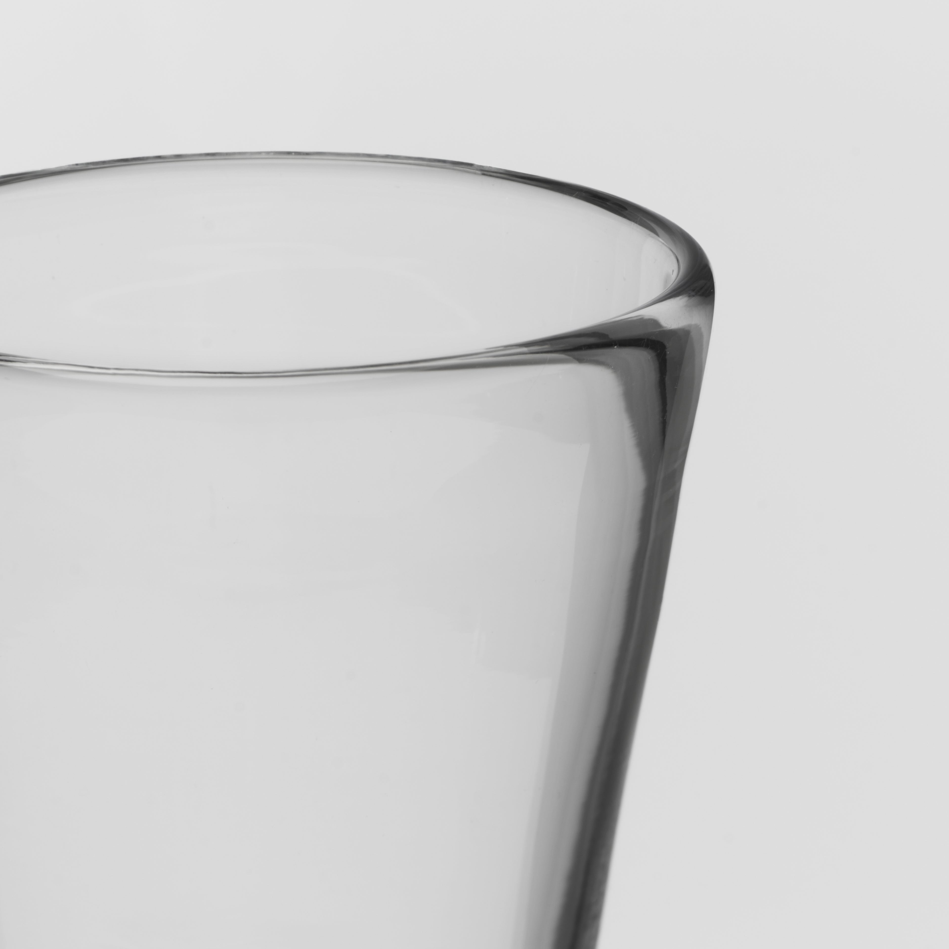 Close-up of a clear glass tumbler with a thick, tapered base on a light gray background.
