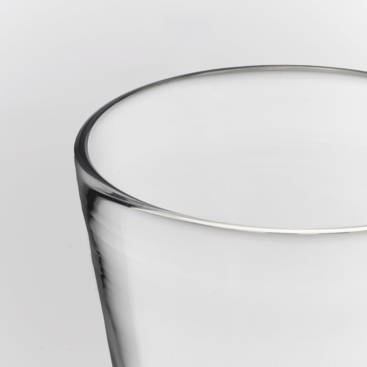 Close-up of a clear glass tumbler showing the rim and part of the body against a light gray background.
