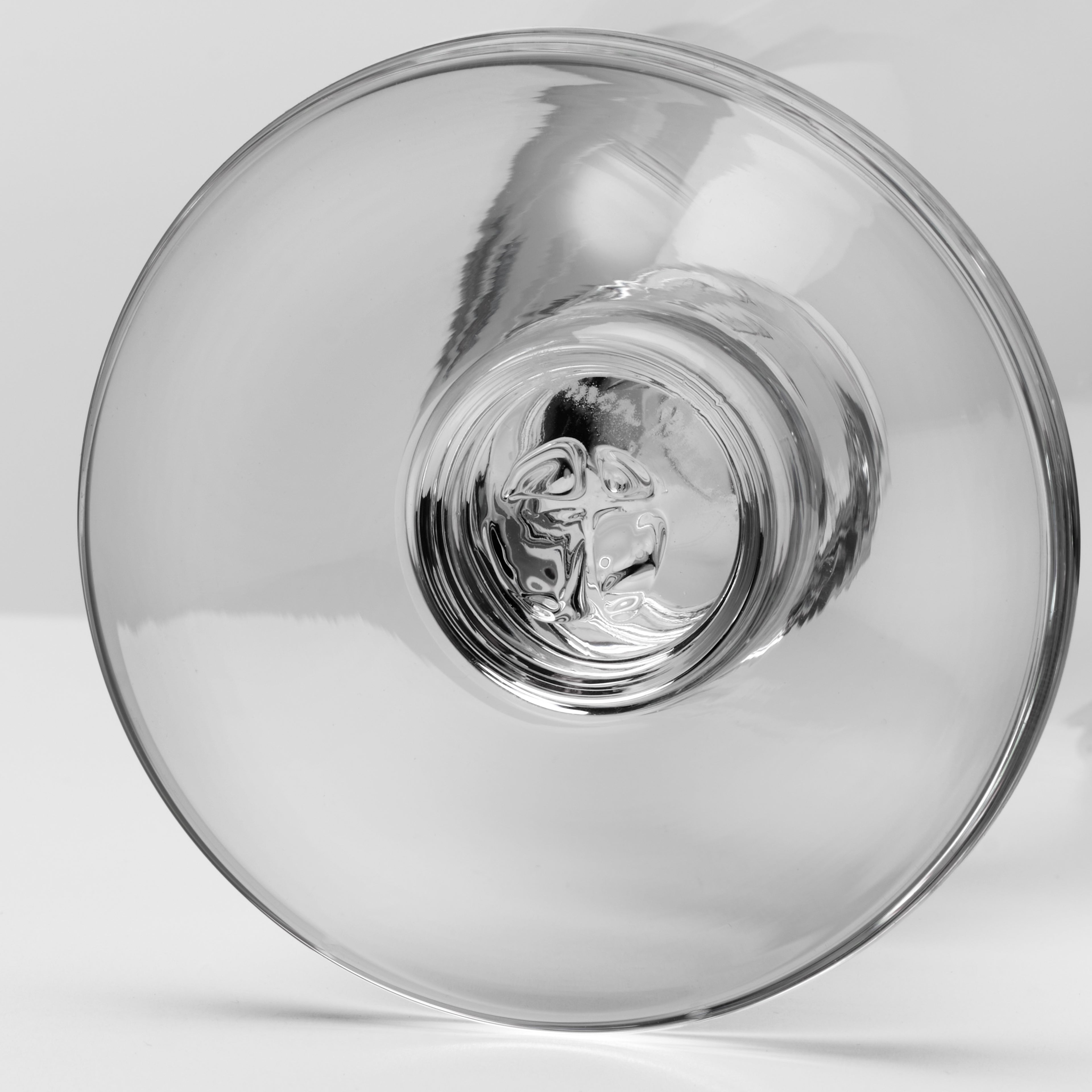 A clear glass goblet or tumbler shown from the bottom photographed on a clean light gray to white studio background.