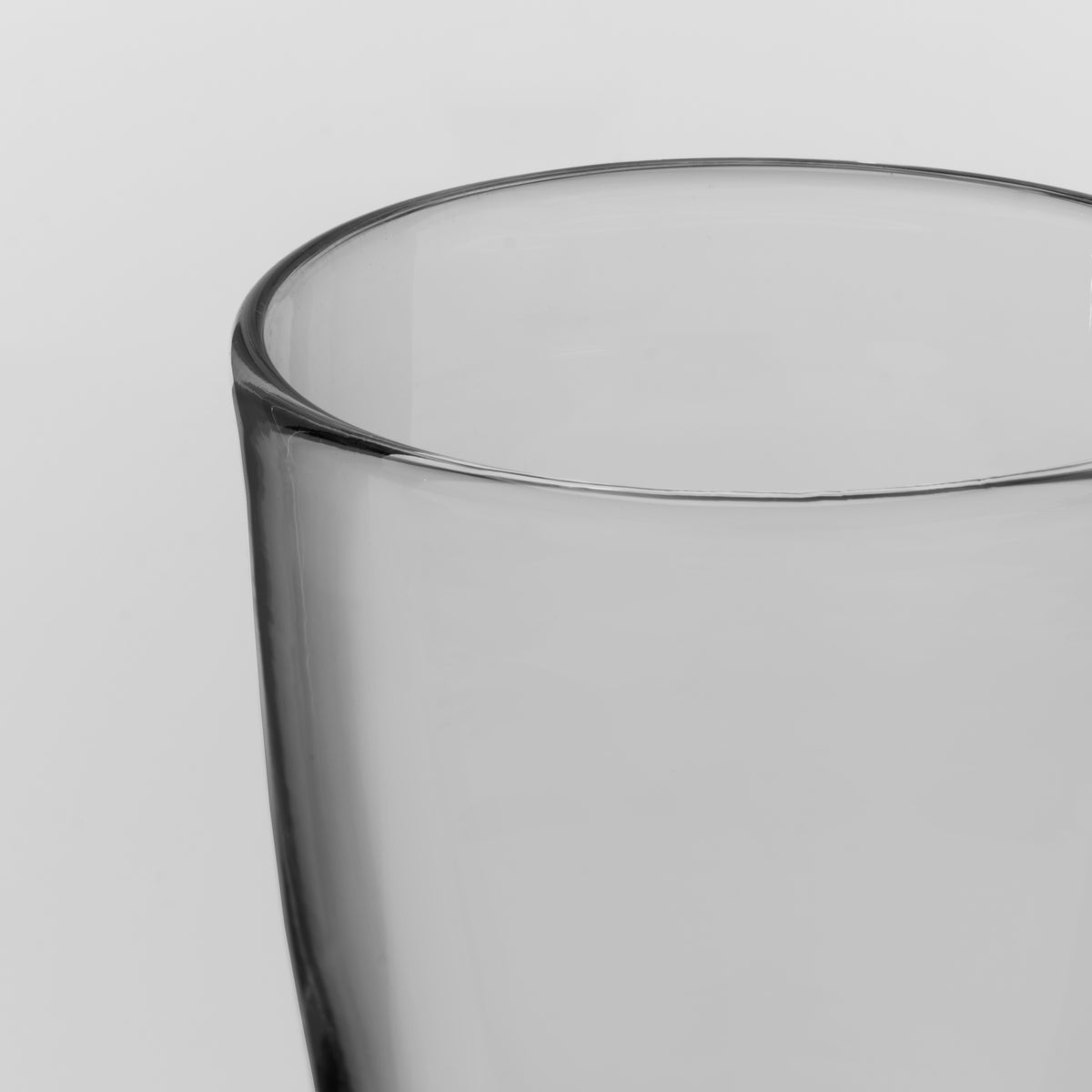 Close-up of a clear glass tumbler with a thick, rounded rim on a light gray background.