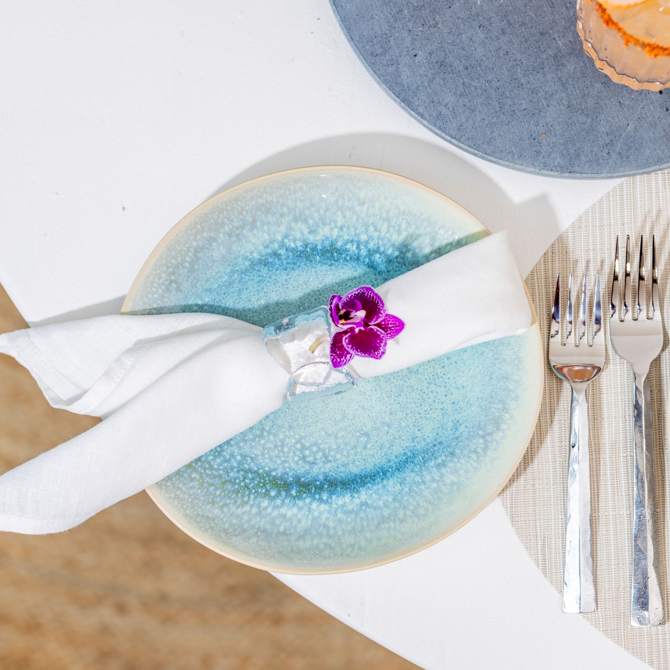 Two round plates with blue-to-white gradient glaze, white napkin, and silverware arranged on a place setting.