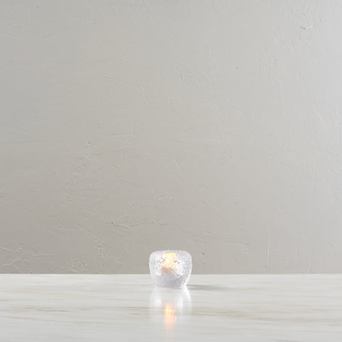 White spherical tealight holder with lit candle inside, displayed on light wooden surface.