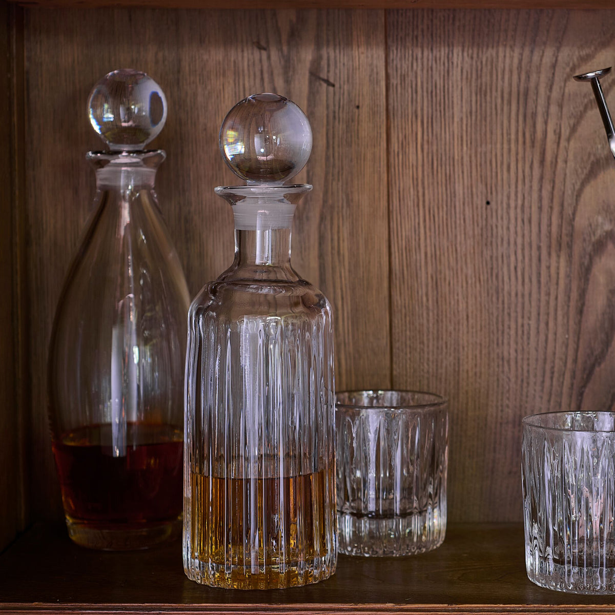 Clear glass decanter with spherical stopper and vertical fluting, displayed with matching glasses containing amber liquid.