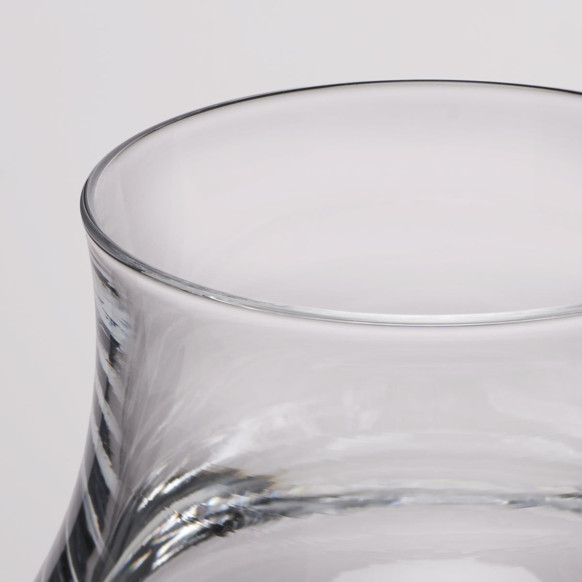 Close-up of a clear glass with a flared rim and subtle spiral texture on the lower body, photographed against a light gray background.