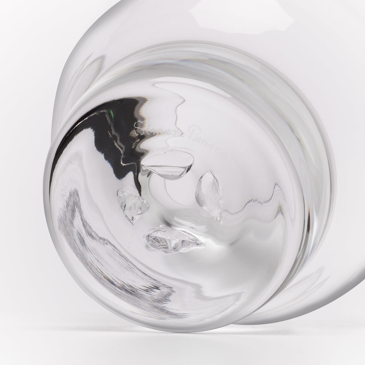 A close-up studio shot of a clear glass, showing the curved transparent surface and reflective highlights against a white background.