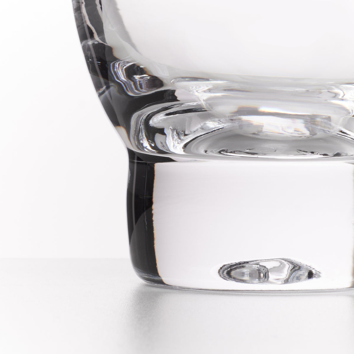 Close-up of a clear glass tumbler with a thick, rounded base on a white background.