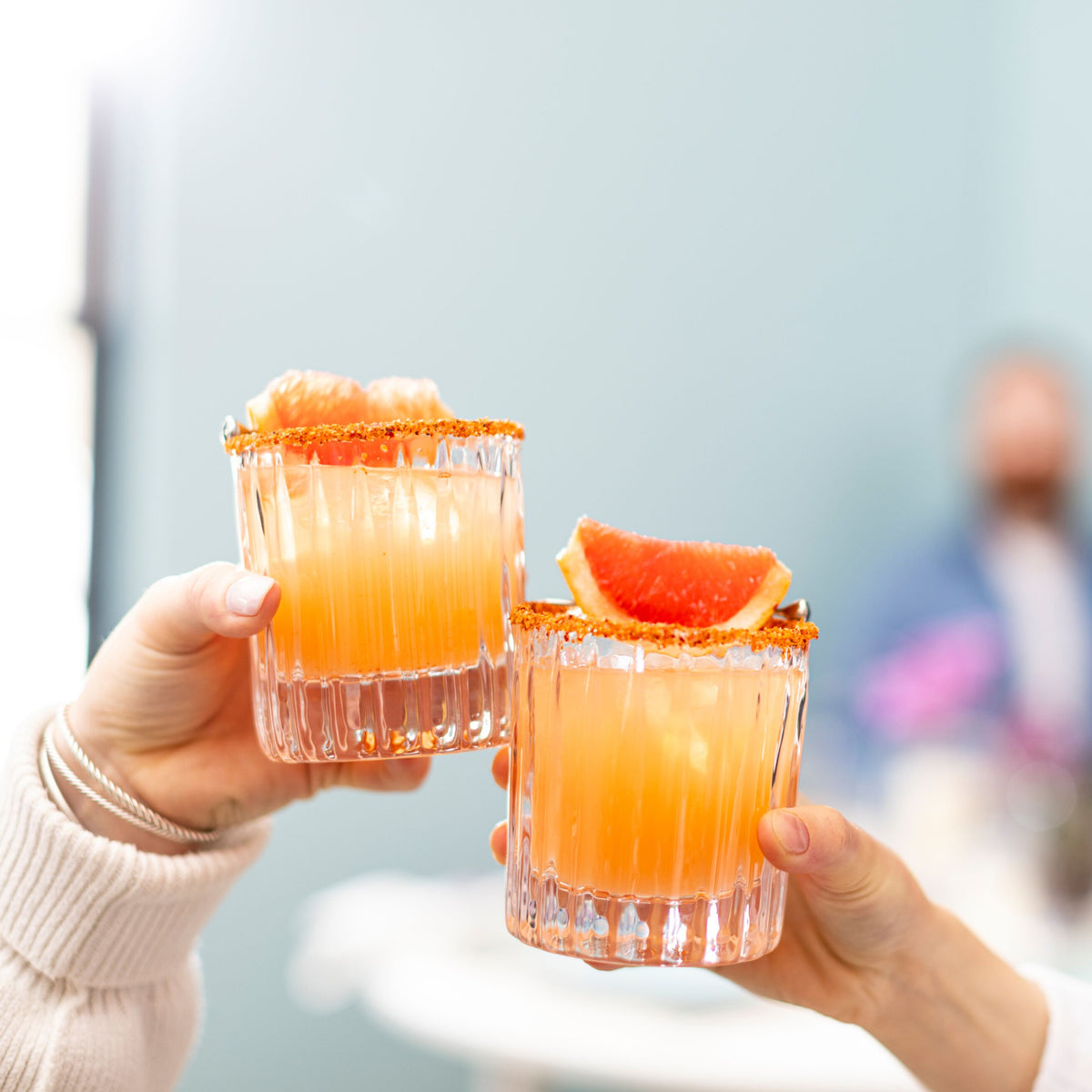 Two crystal double old-fashioned glasses filled with orange cocktails, garnished with sugar rims and grapefruit slices.