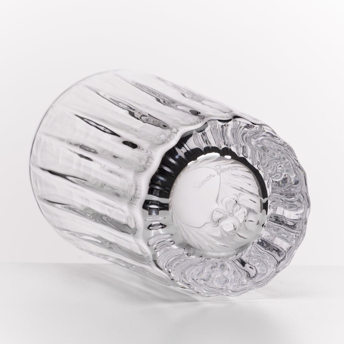 A clear cut-glass tumbler with a ribbed fluted body and a patterned circular base, photographed on a clean white background.