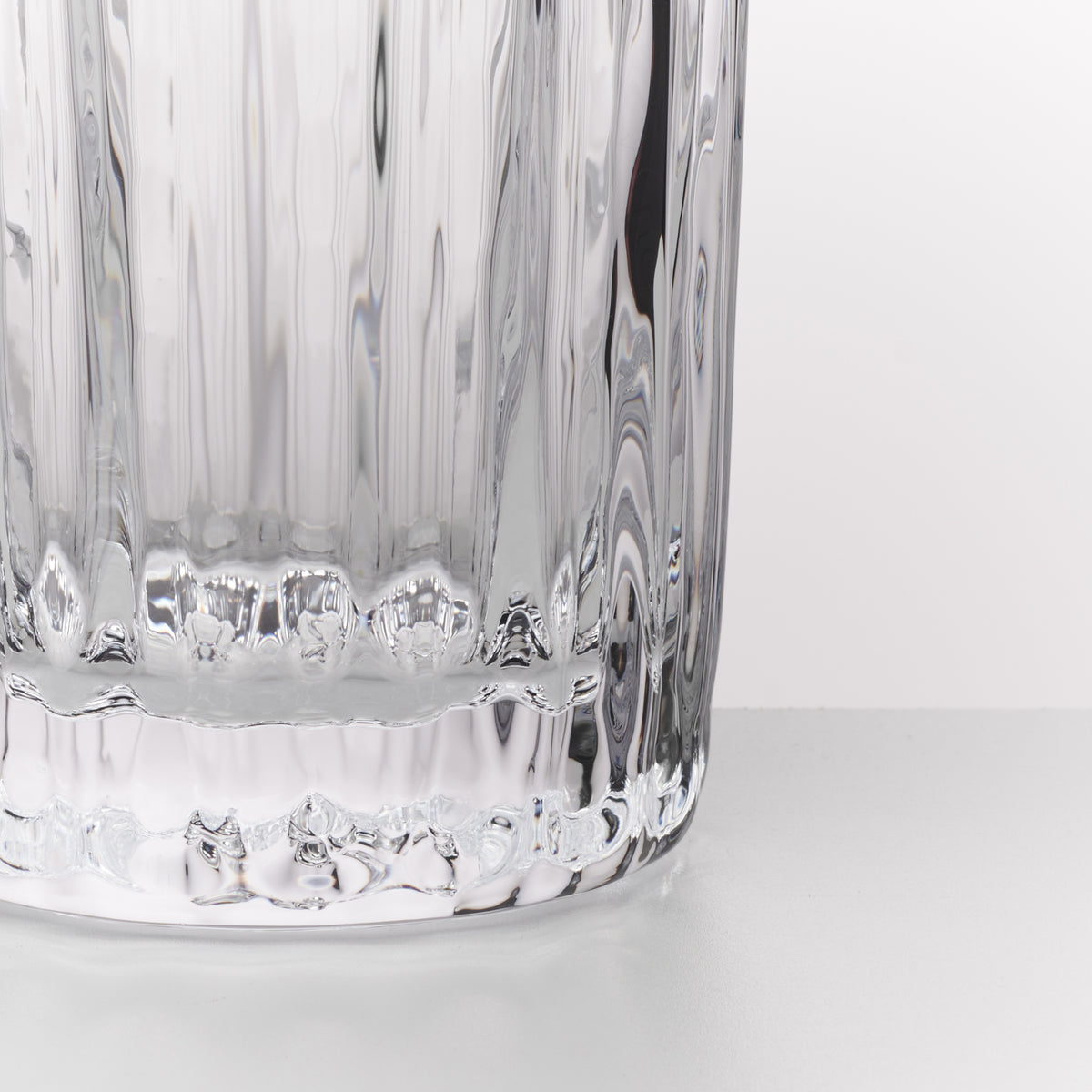 Close-up of a clear ribbed glass tumbler with a textured base, shown against a plain white background.