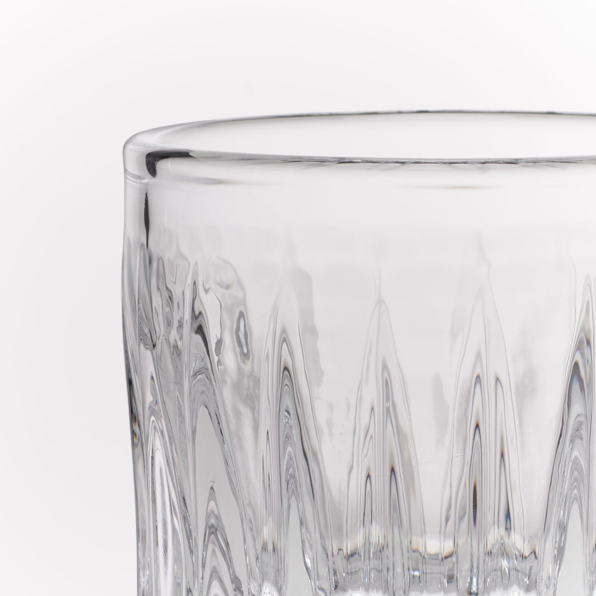 Close-up of a clear textured glass tumbler with a faceted, wavy pattern on a white background.