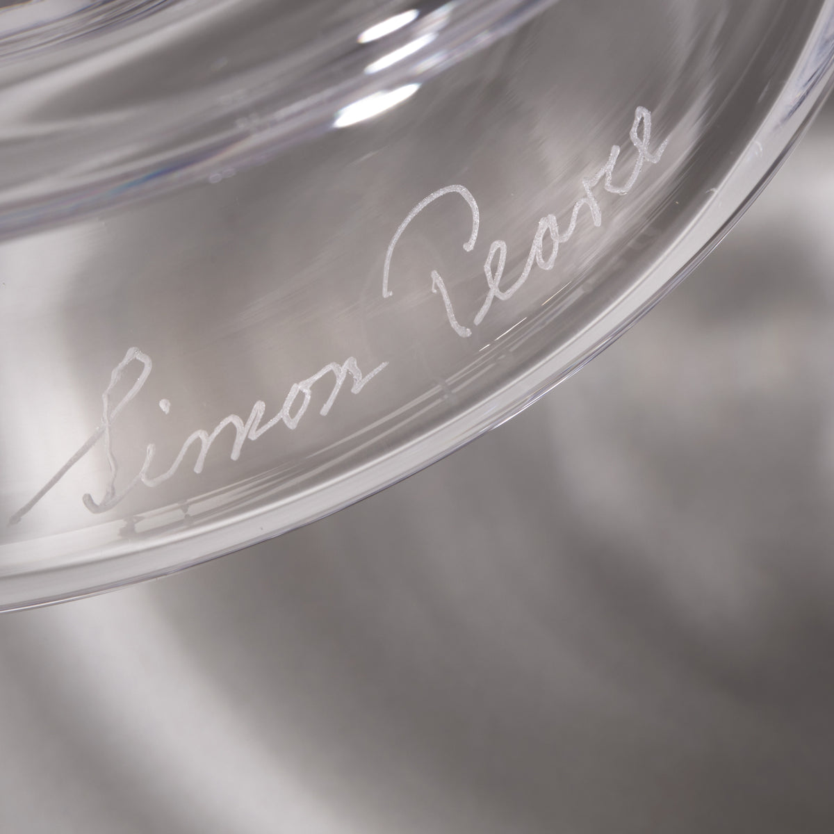 Clear glass hurricane with cursive signature etched on the surface.