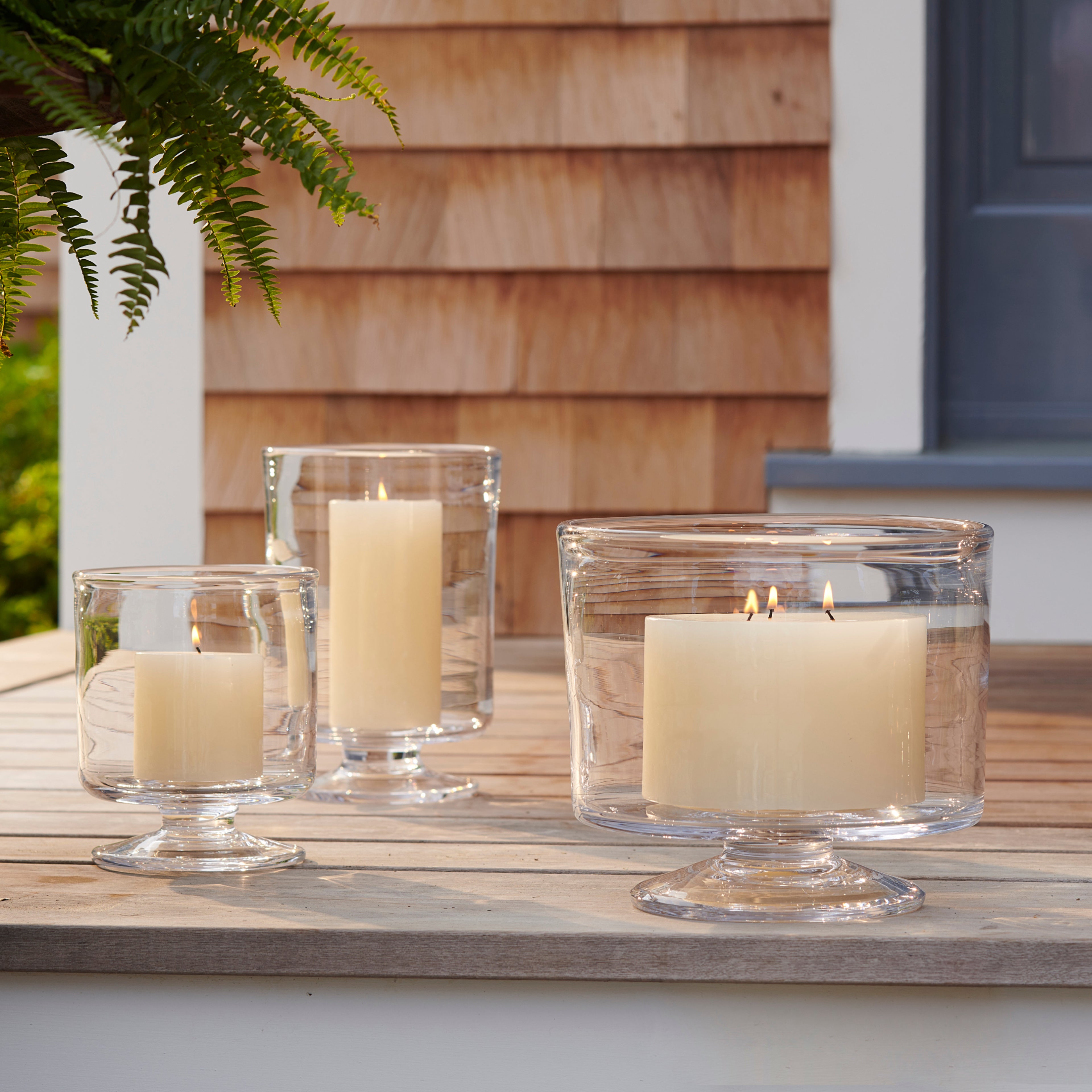 Three cream-colored pillar candles in clear glass hurricane holders of varying heights on a wooden surface.