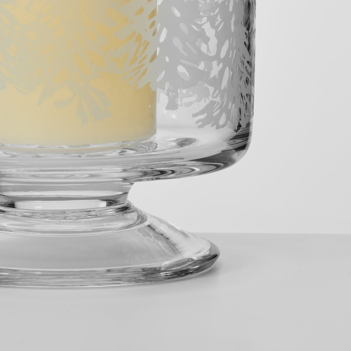 Clear glass hurricane candle holder with engraved forest leaf pattern and pedestal base.
