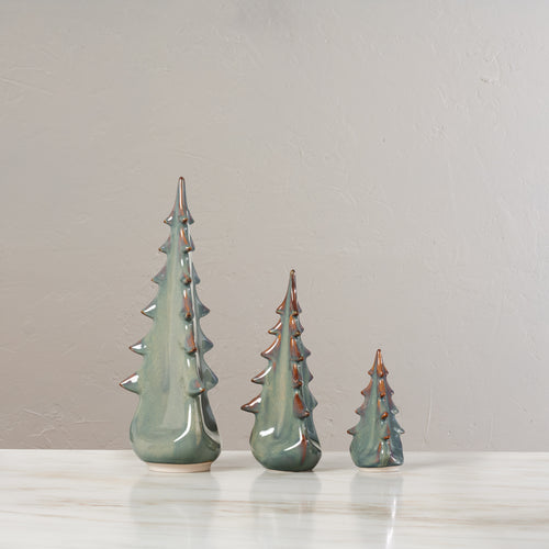 Three ceramic evergreen tree figurines in moss green glaze with metallic accents, arranged by size.