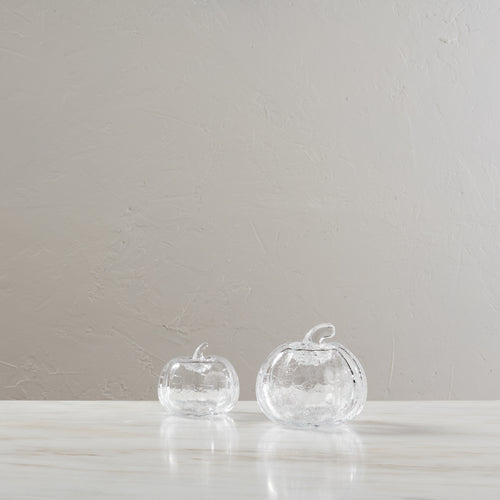 Two clear glass pumpkins with textured crackle finish and stems displayed on a white surface.