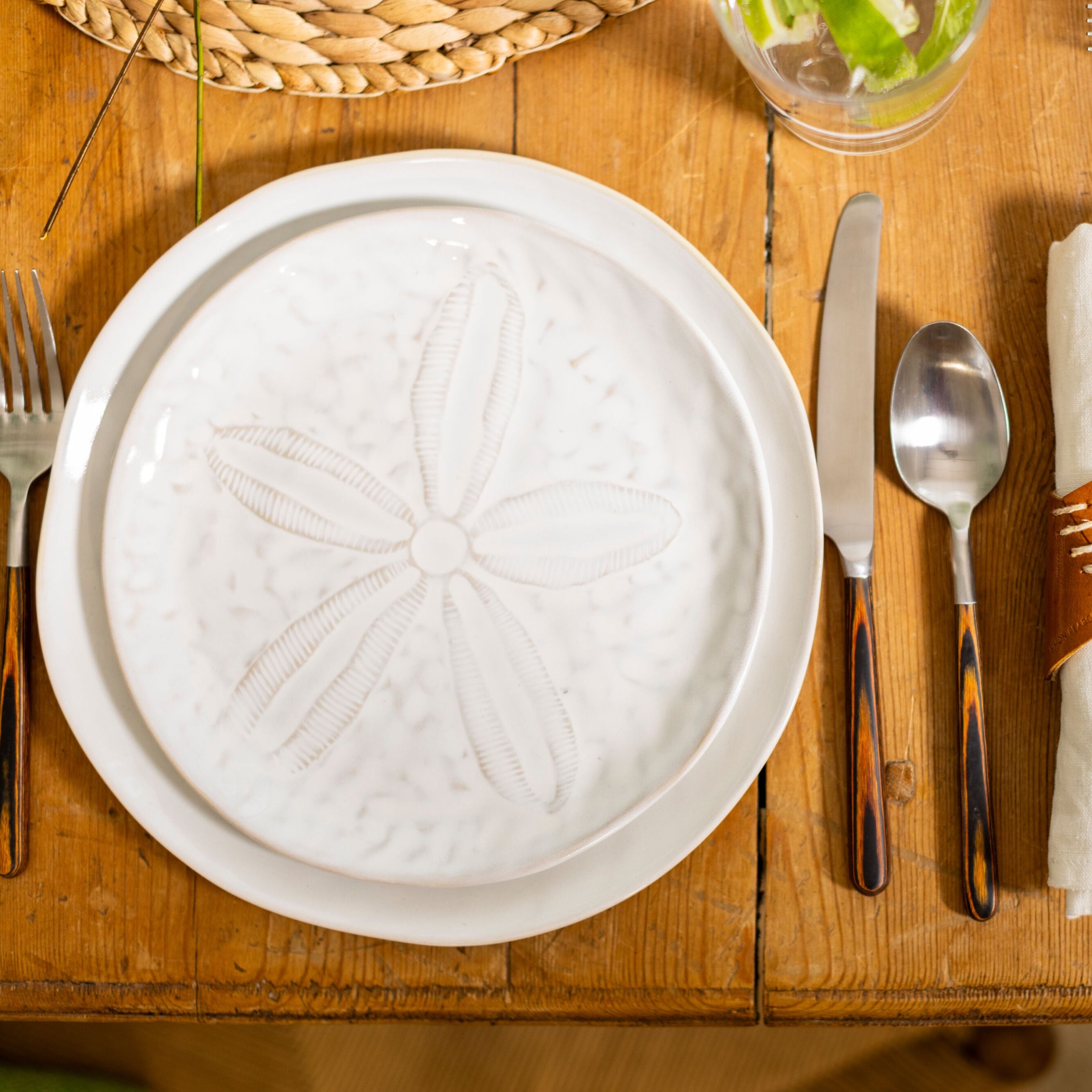 White side plate with embossed sand dollar design, set on wooden table with silverware.