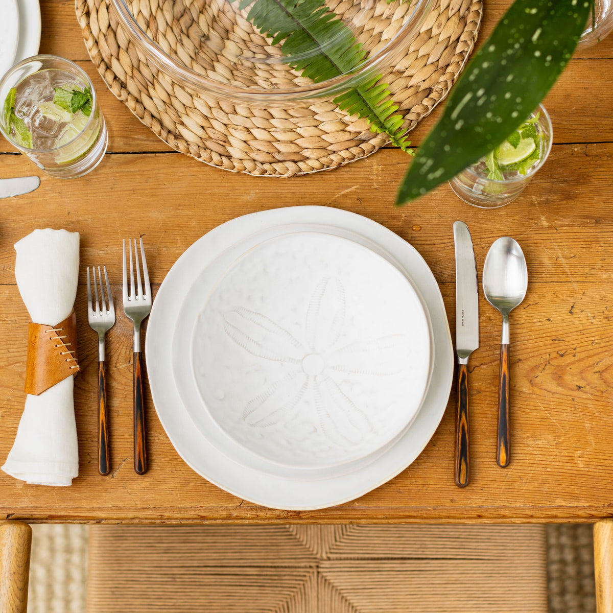 White pasta bowl with subtle sand dollar pattern set on wooden table with place setting.
