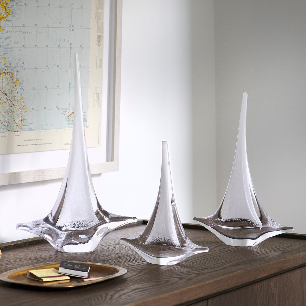 White glass sailboat sculptures with tapered sails and broad bases displayed on wooden surface.
