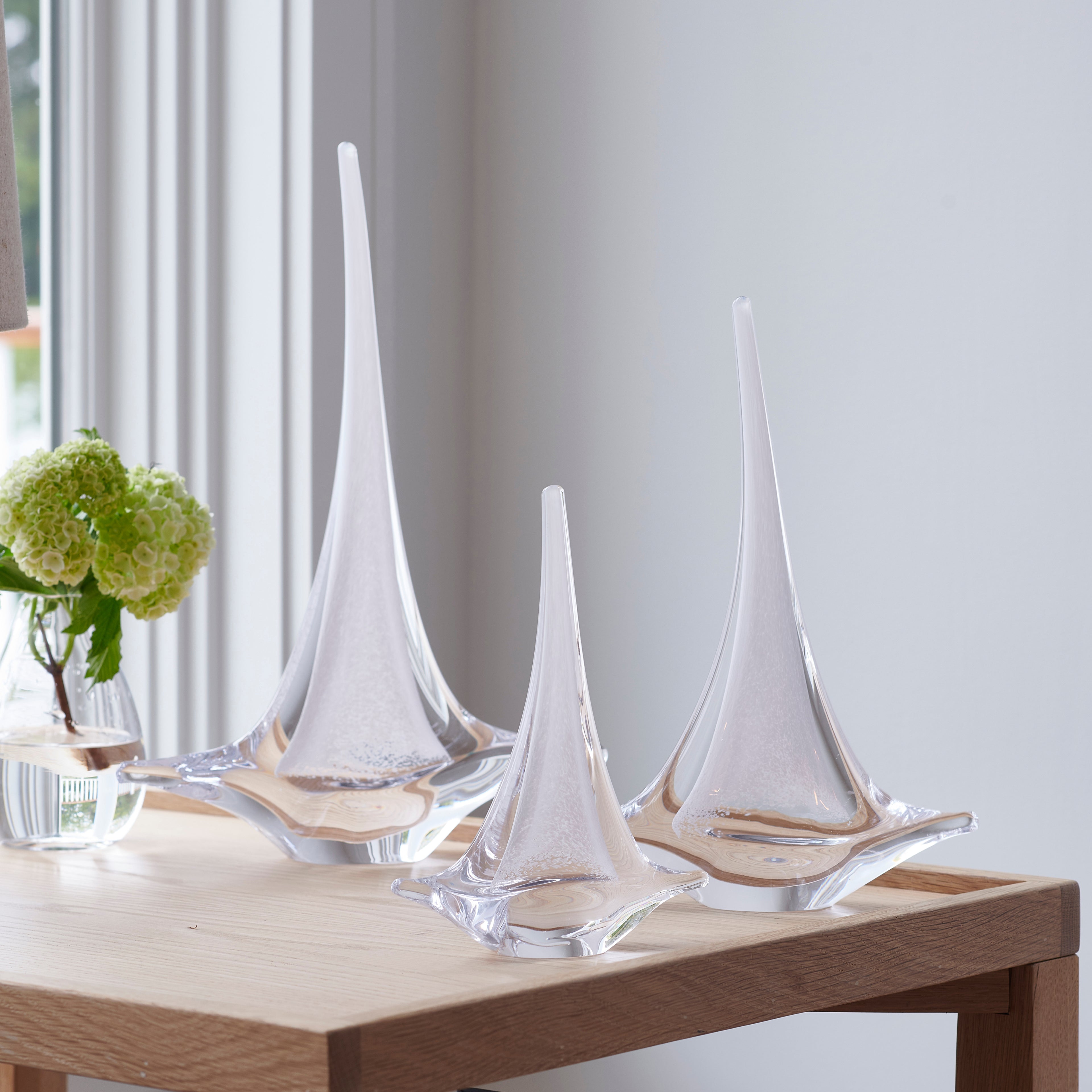 Three white glass sailboat figurines with curved sails on wooden bases, displayed on a table.