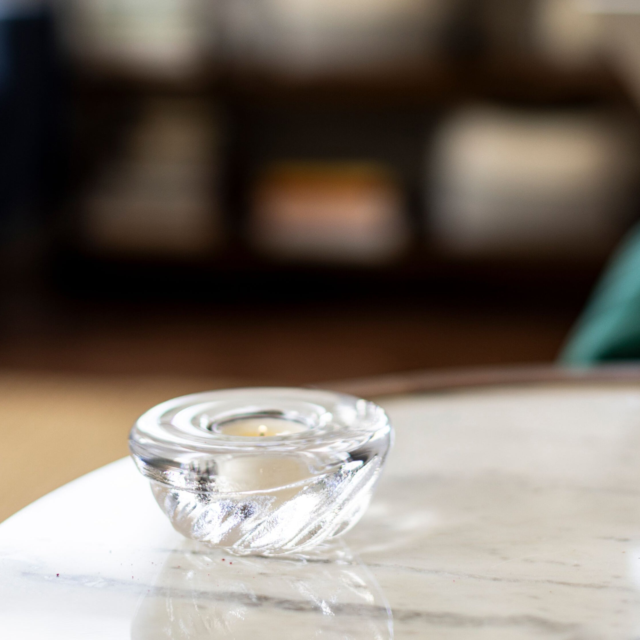 Clear glass shell-shaped tealight holder with cream-colored candle inside, sitting on white marble surface.