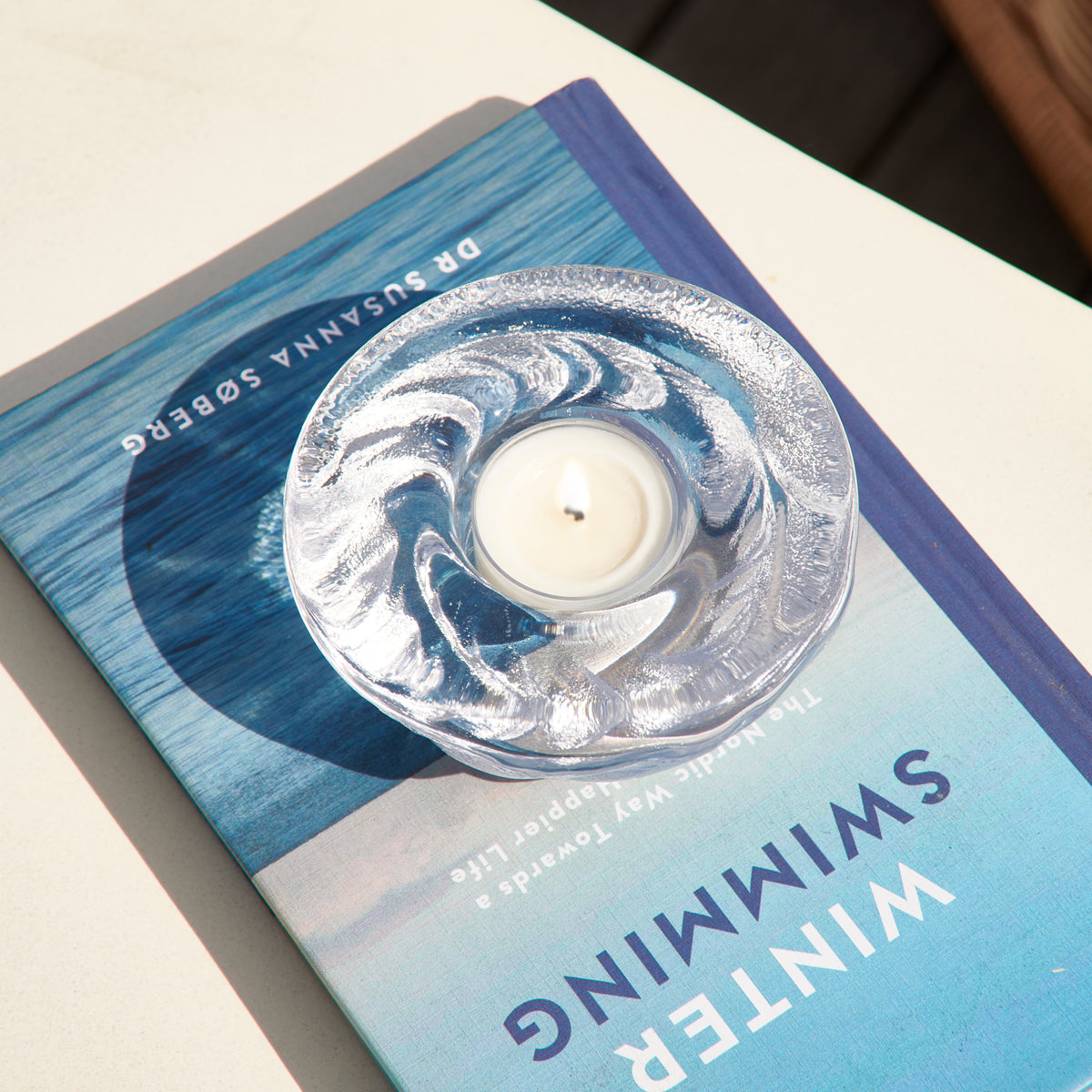 Shell-shaped silver tealight candle in clear container on blue gradient gift box.