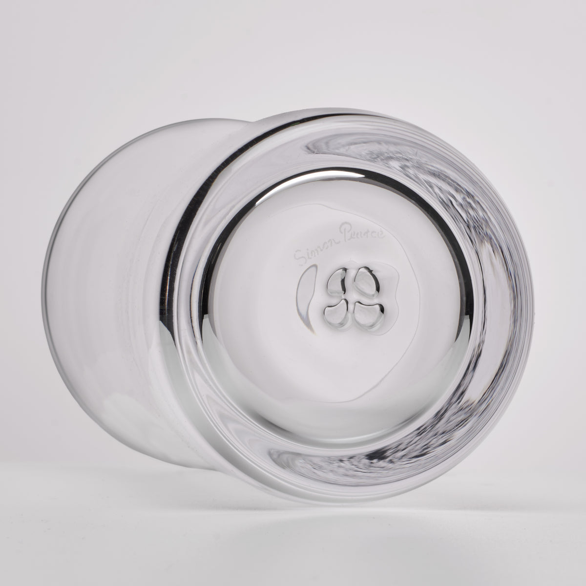 A clear glass tumbler shown from a bottom angle, featuring a thick outer rim and a thickened circular base with a logo and the words 'Simon Pearce' visible in the center.
