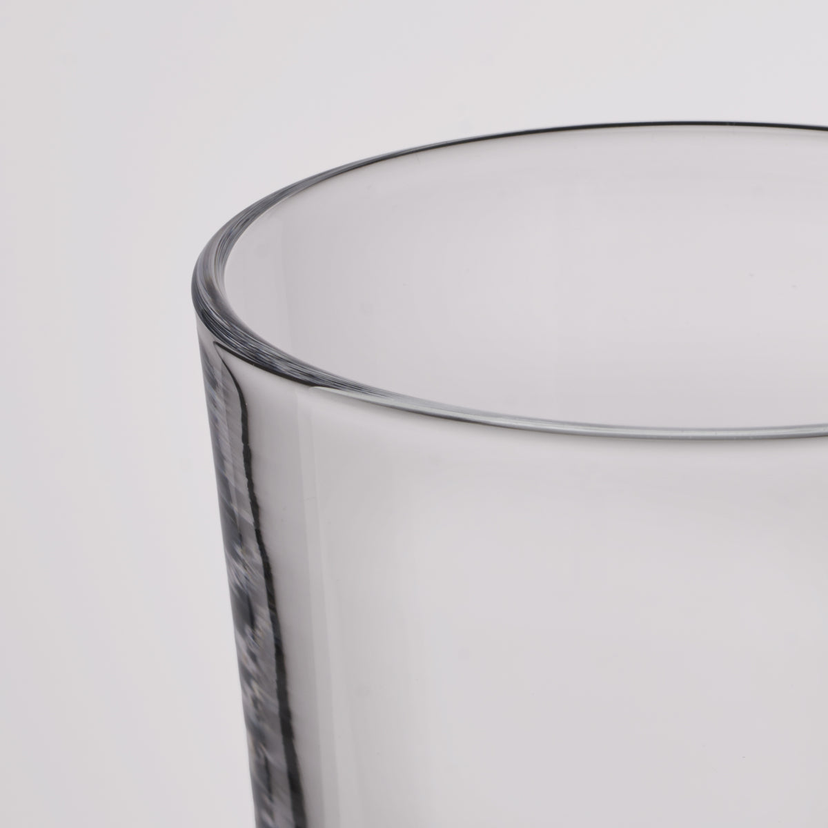 Close-up of a clear glass tumbler showing the rim and part of the textured glass body against a light gray background.