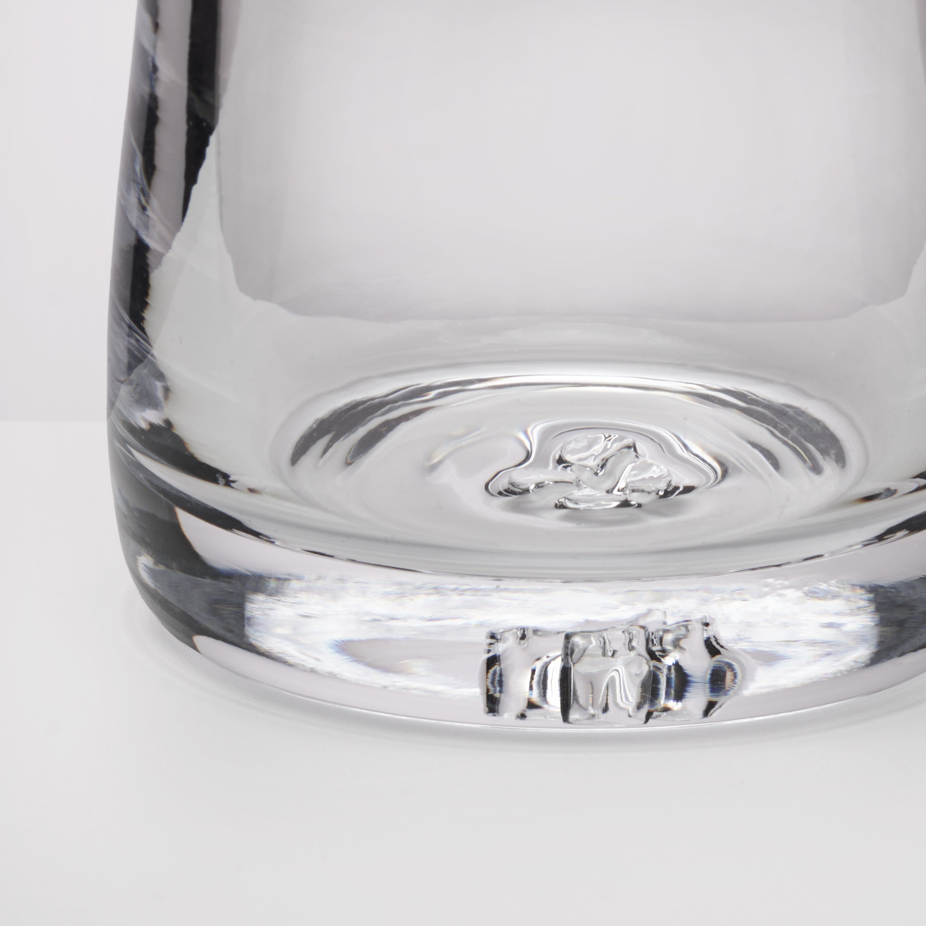 Close-up of the base of a clear glass, showing the transparent glass material and reflective surface on a white background.