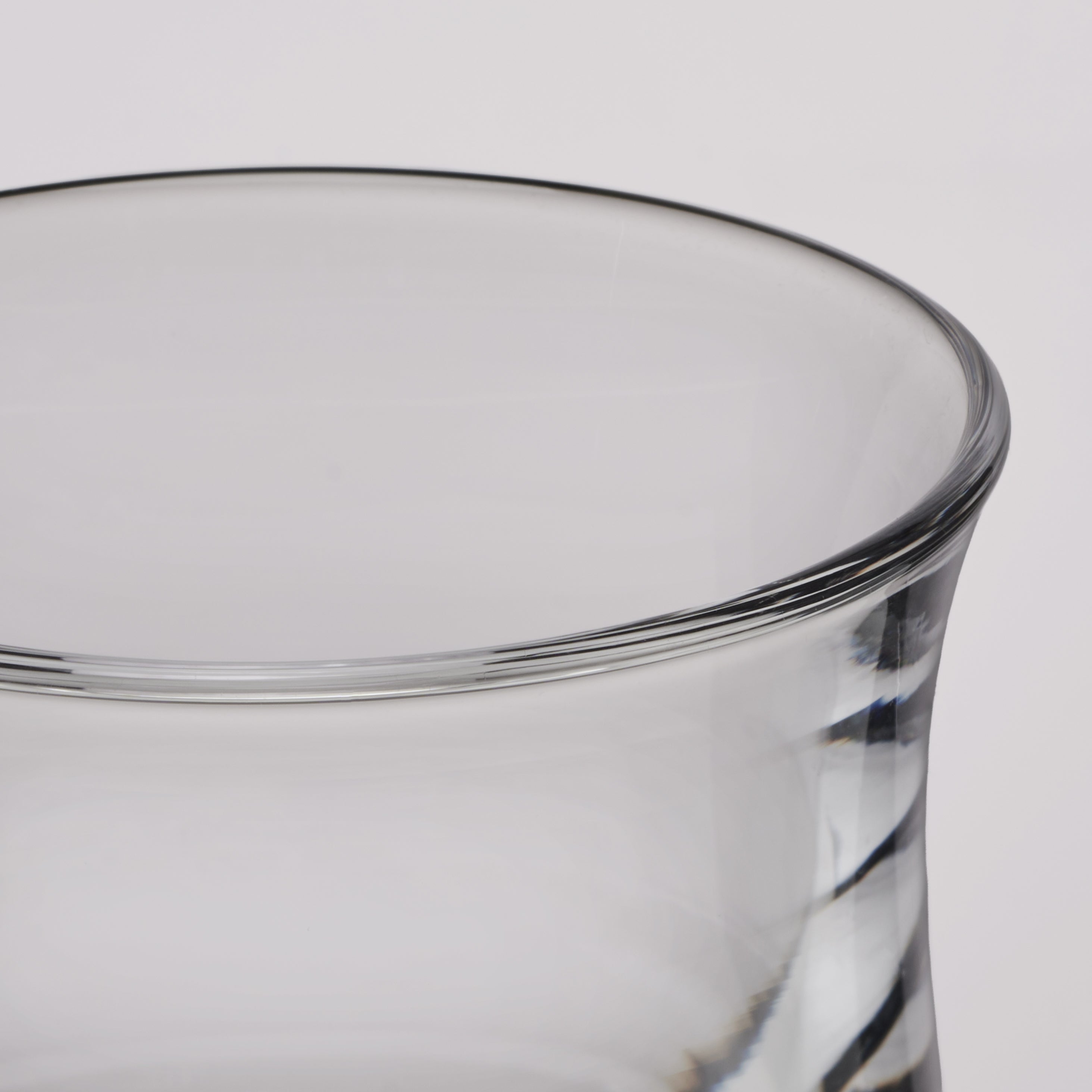Close-up of a clear glass tumbler showing the rim and part of the twisted glass body against a light gray background.