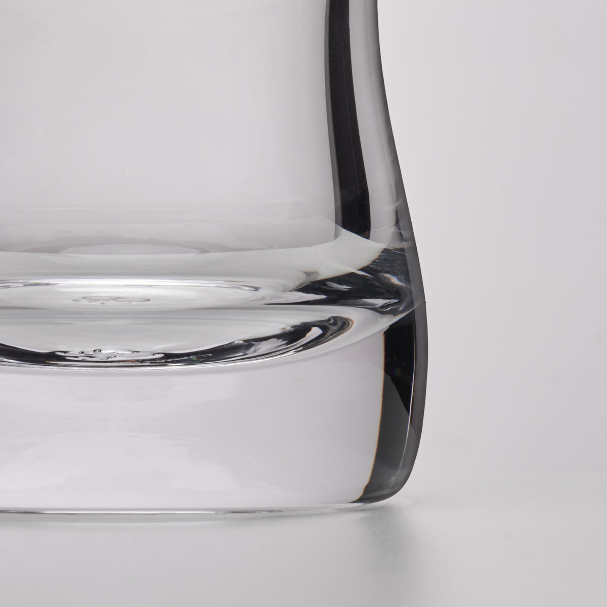 Close-up of a clear glass decanter showing the base and curved rim against a light gray background.