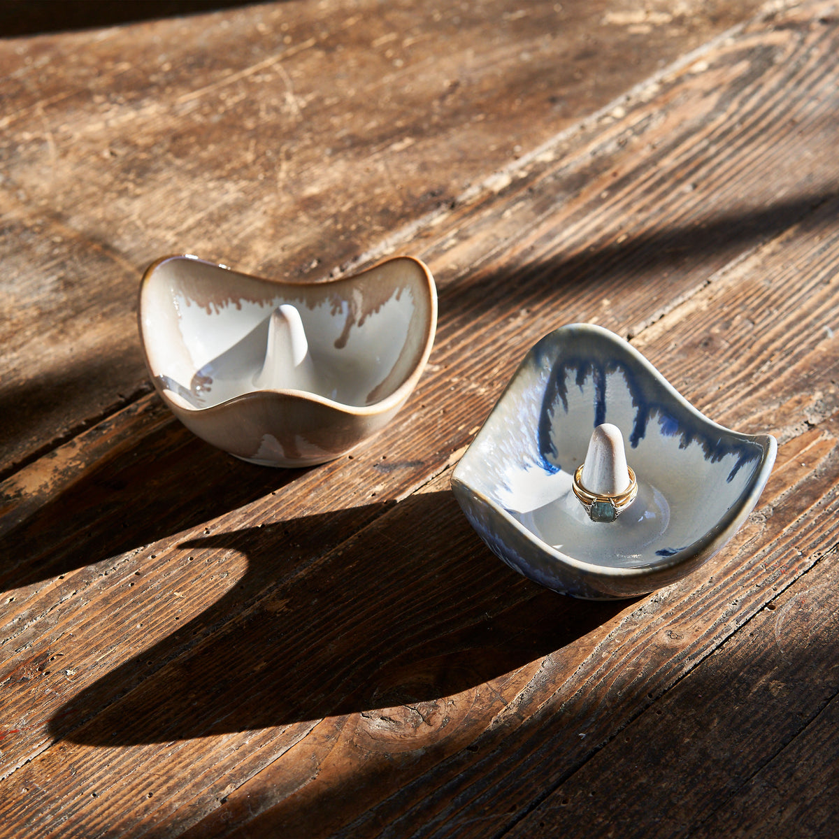Two ceramic ring holders with central posts in white and blue glaze on weathered wood surface.