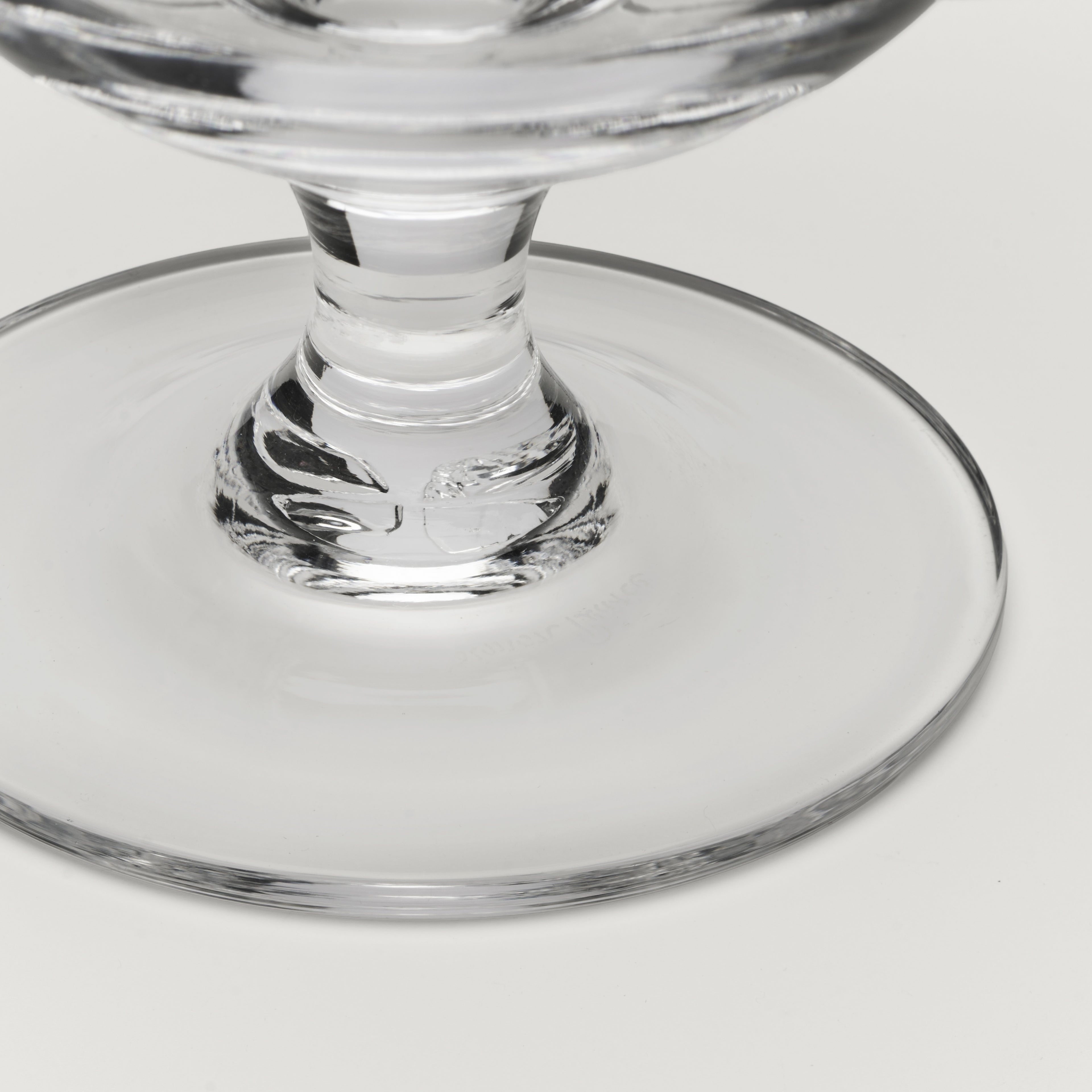 Close-up of a clear glass pedestal bowl or cup base on a light gray background.