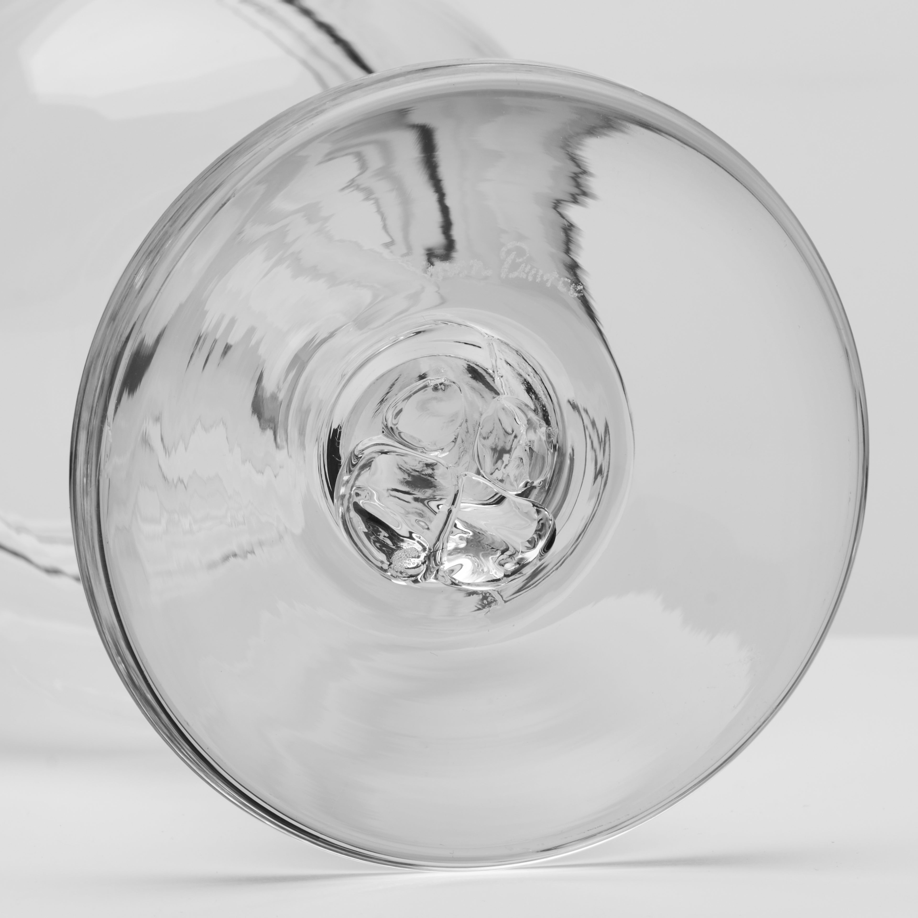 A close-up of a clear glass wine glass showing the circular base photographed on a light gray background.