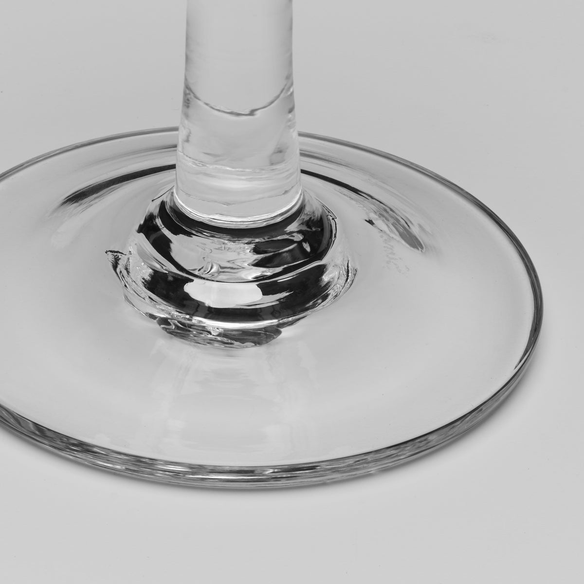 Close-up of the base and stem of a clear glass wine glass on a light gray background.