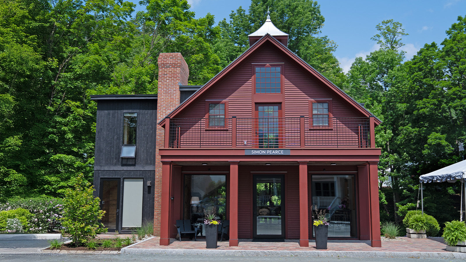 Exterior of the Simon Pearce retail store in Stowe, Vermont, housed in a red barn-style building with black trim and large windows, surrounded by trees