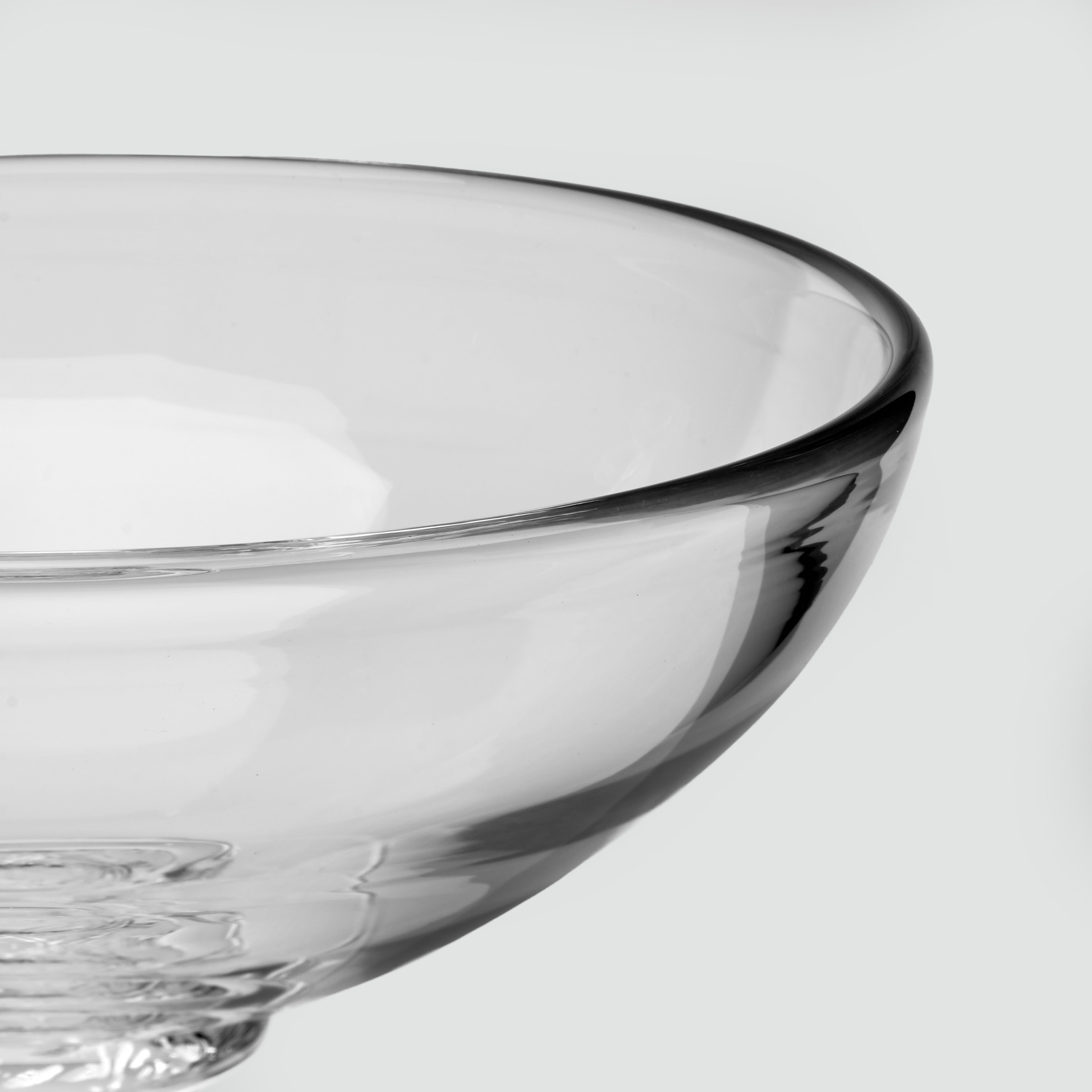 Close-up of a clear glass bowl with a thick rim and pedestal base, photographed against a light gray background.
